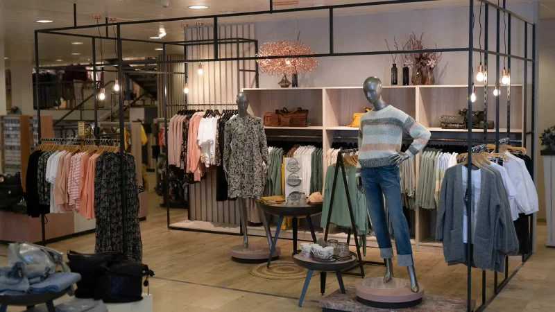 Pop-up-Fläche im Modehandel mit schwarzem modustore-Rahmensystem, Kleiderstangen, Wandregal und zwei Schaufensterpuppen